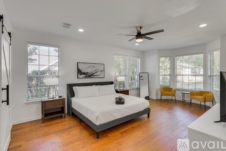 A bedroom with a large bed, a ceiling fan, and a painting on the wall.