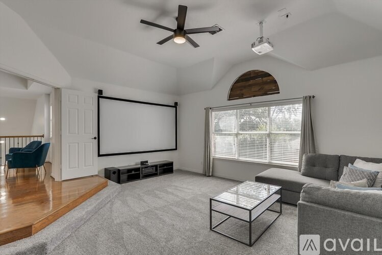 A living room with a grey sofa, a coffee table, and a large screen on the wall.