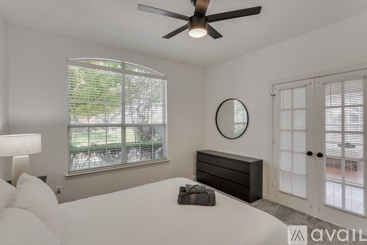 A bedroom with a large bed, a ceiling fan, and a window with blinds.
