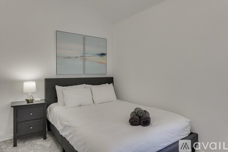 A bedroom with a large bed, a nightstand with a lamp, and a picture on the wall.