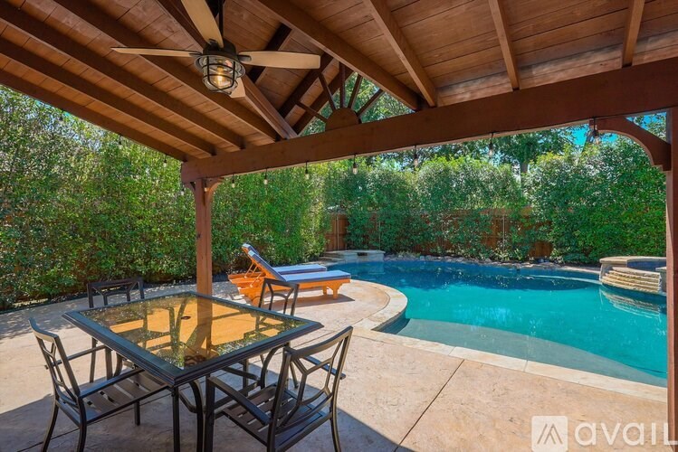 A table and chairs are set up on a patio with a pool in the background.