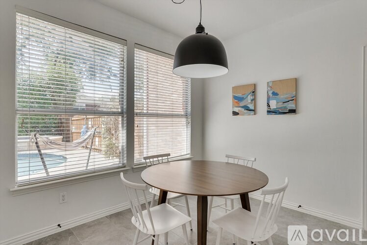 A dining room with a table and chairs and a hammock outside the window.