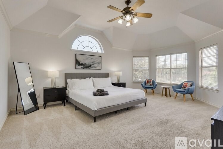 A bedroom with a large bed, a ceiling fan, and a window with a view.