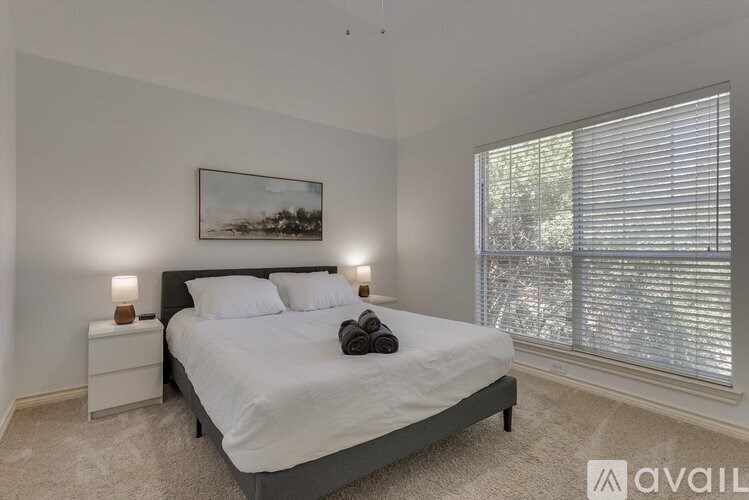 A bedroom with a large bed, two lamps, and a painting on the wall.