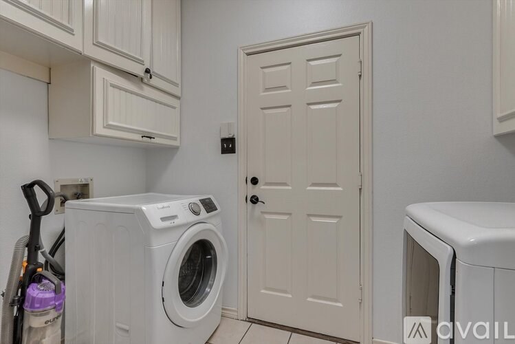 A white washing machine sits in a laundry room with a white door and white cabinets.