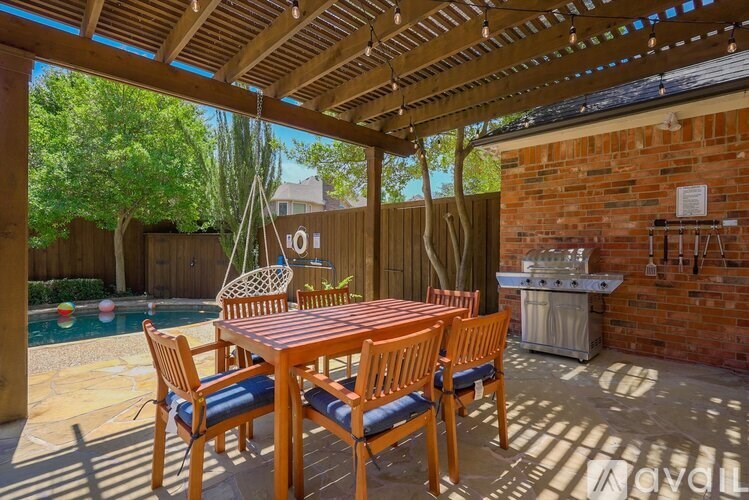 A wooden table and chairs are set up on a patio with a pool in the background.