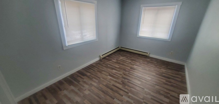 A room with wooden flooring and two windows.