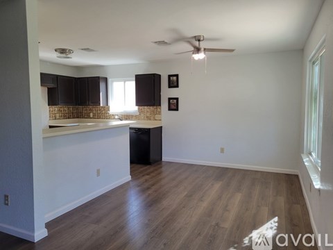 A room with a ceiling fan and a kitchen area with a counter and cabinets.