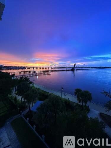 A beautiful sunset view of a pier extending into the water with trees in the foreground.