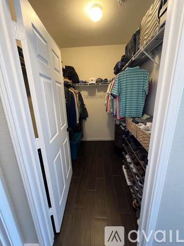 A white closet with clothes hanging on shelves and a white door.