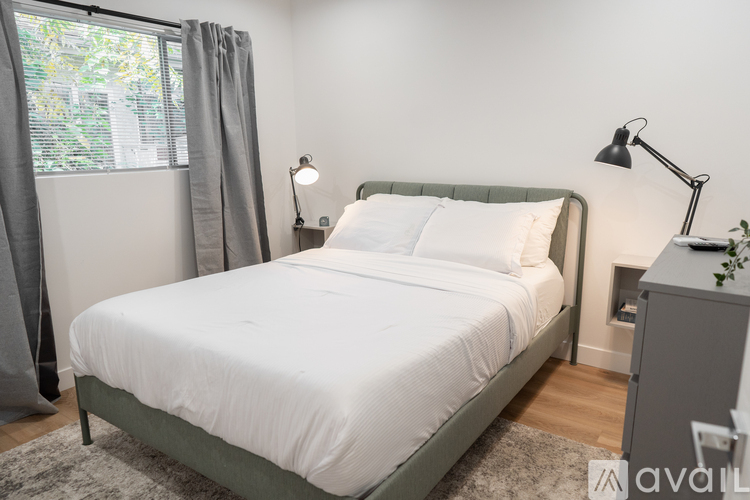 A bed with a white comforter and two white pillows sits in a room with a grey headboard and a grey nightstand with a plant on top.