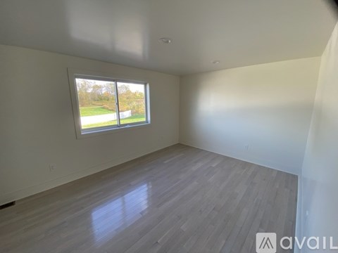 A room with a large window and wooden flooring is available for rent.