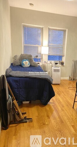 A bedroom with a bed, a blue blanket, a white air conditioner, and a window with blinds.
