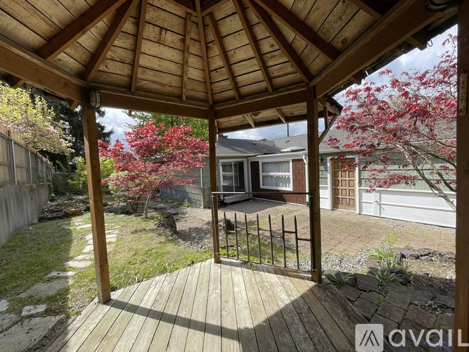 A wooden gazebo with a metal gate in the foreground and a house in the background.