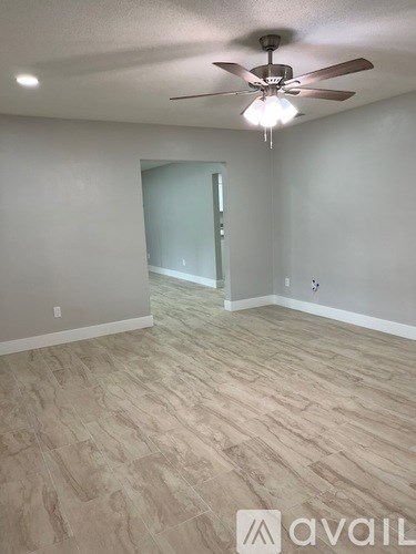 A room with a ceiling fan and light fixture, and a door on the left.
