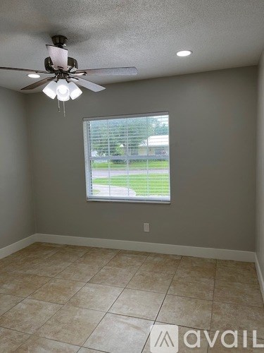 A room with a ceiling fan and a window overlooking a green field.