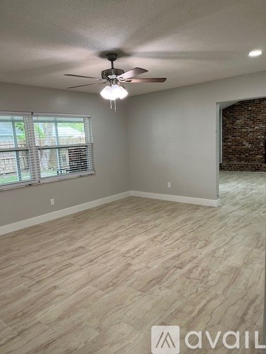 A room with a ceiling fan and light, wooden flooring, and a window with blinds.