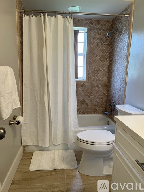 A white toilet sits in a bathroom with a white shower curtain.
