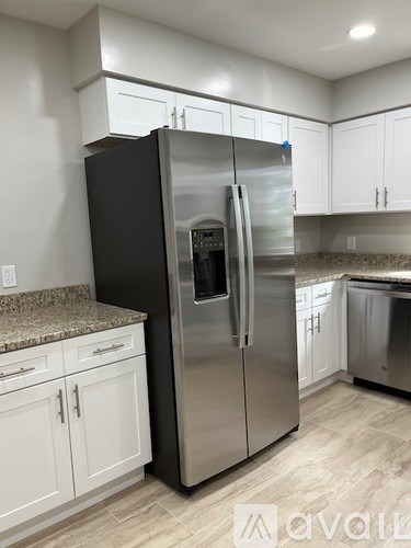 A black refrigerator stands in a kitchen with white cabinets.
