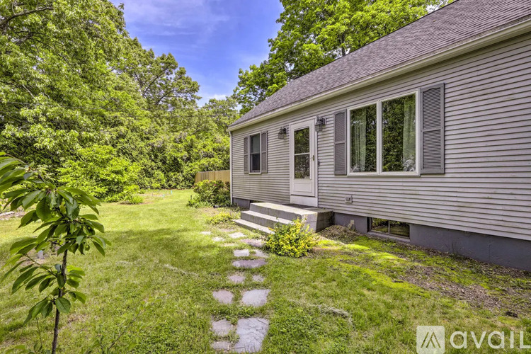 A house with a grey siding and a small porch is surrounded by a grassy area and trees.
