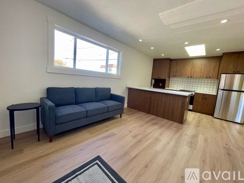 A living room with a grey sofa and a kitchen area with a refrigerator in the background.