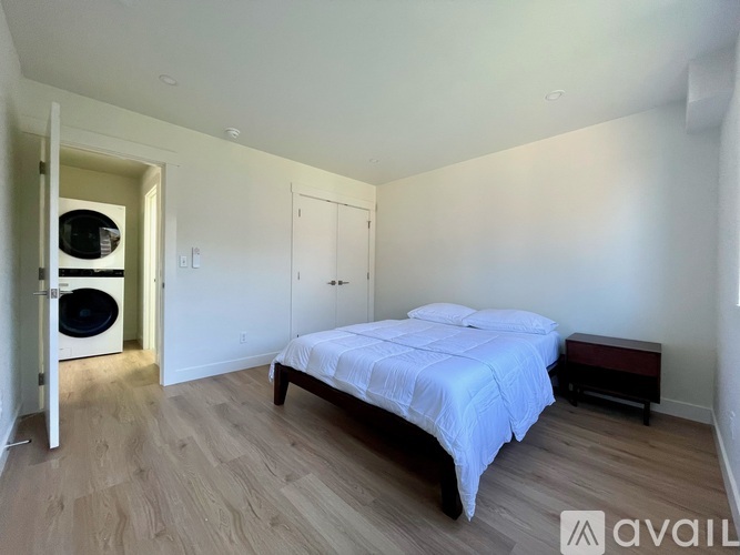 A bedroom with a bed, a bench, and a washing machine in the corner.