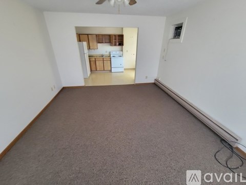 A spacious room with a carpeted floor and a view of a kitchen area in the distance.