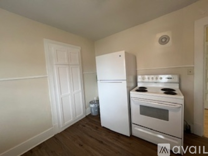 A white refrigerator and stove in a kitchen with wooden floors and white walls.