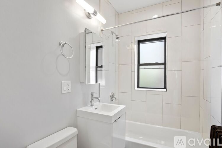 A white bathroom with a tub, sink, mirror, and light.