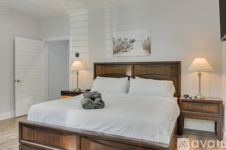 A bedroom with a large bed, two lamps, and a painting on the wall.