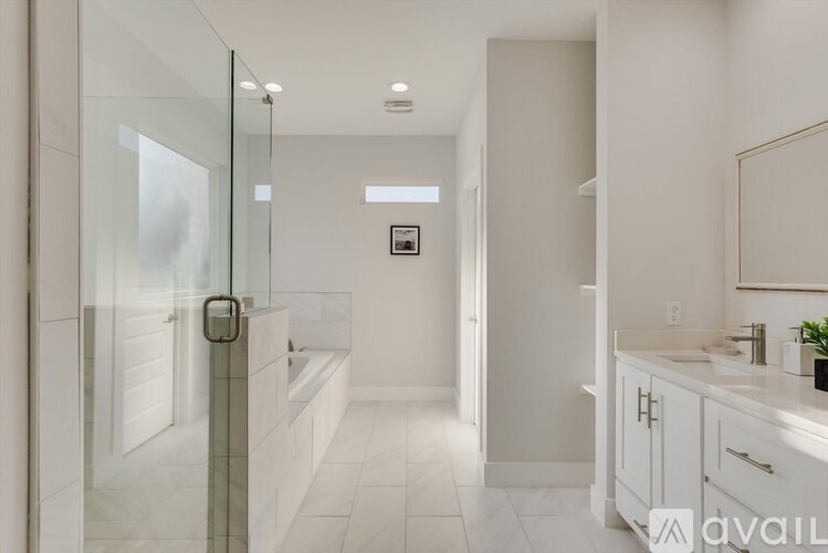A bathroom with a glass shower door and white cabinets.