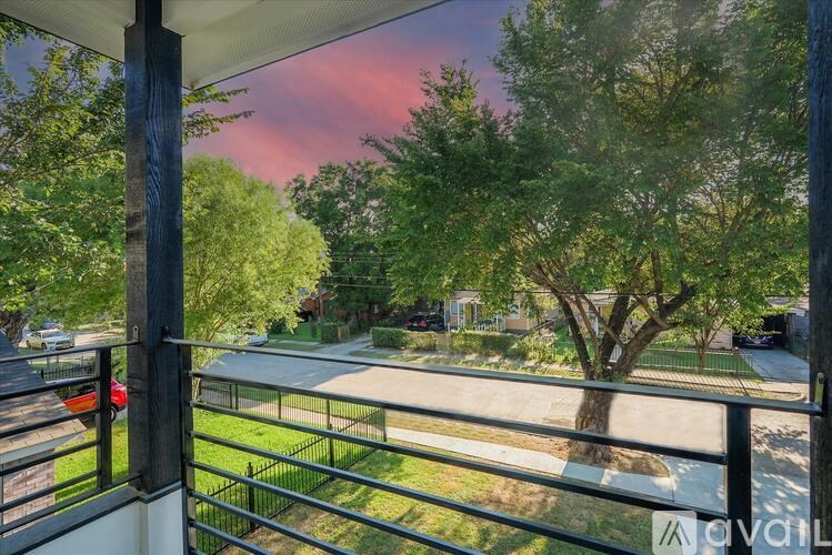A balcony with a metal railing overlooks a tree and a street.