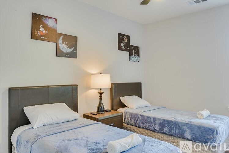 A bedroom with two beds, one of which is made, and a lamp on a bedside table.