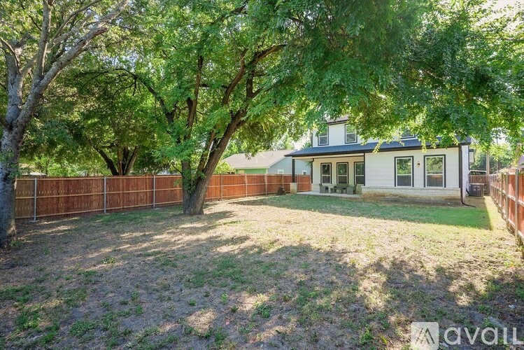 A house with a white facade and a brown fence is surrounded by trees.