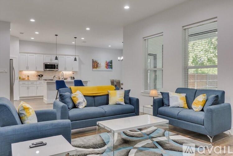 A modern living room with a grey sofa, a glass coffee table, and a kitchen area in the background.