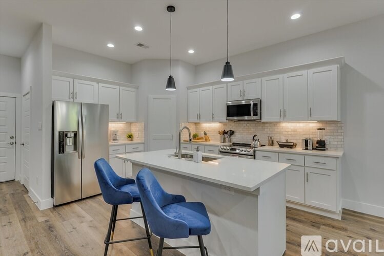 A kitchen with white cabinets and a white island with blue chairs.