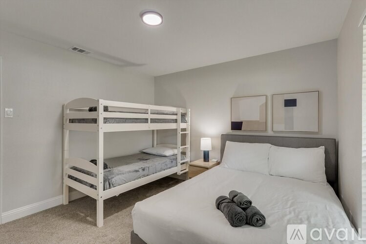 A bedroom with a white bed, two bunk beds, and a nightstand with a lamp.