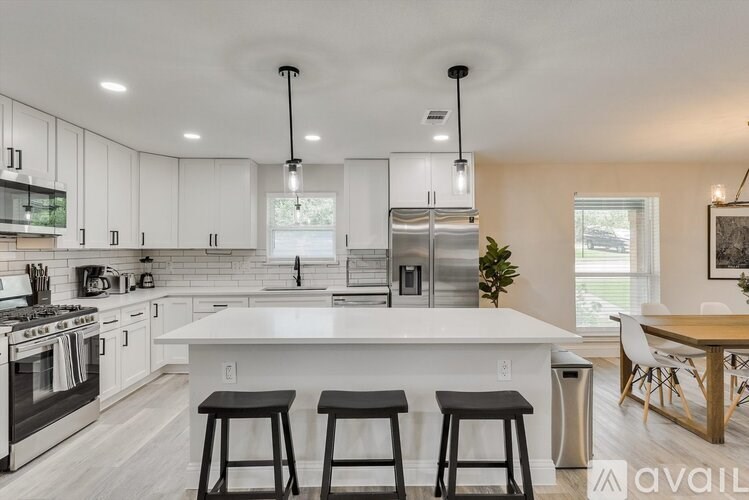 A kitchen with white cabinets and a white island with three bar stools.