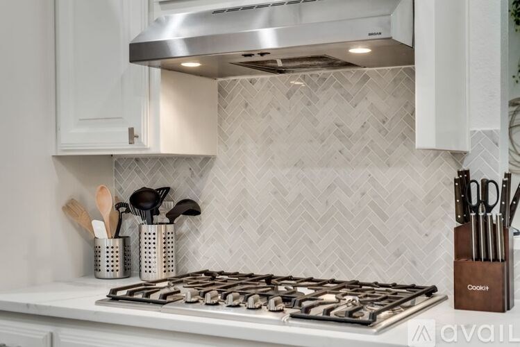 A modern kitchen with a white stove top and a silver range hood.