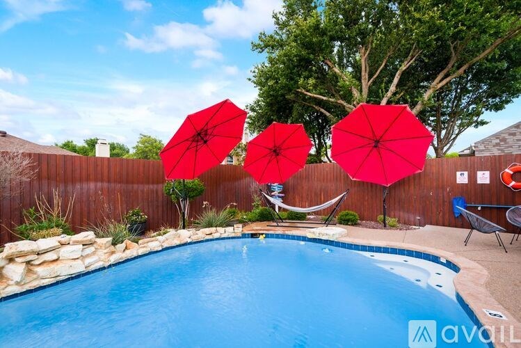 A pool with a hammock and two red umbrellas.