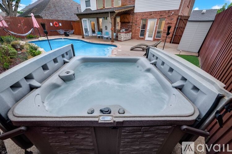 A hot tub is in the foreground of a backyard with a pool and patio area.