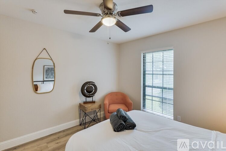 A bedroom with a bed, chair, and a fan.