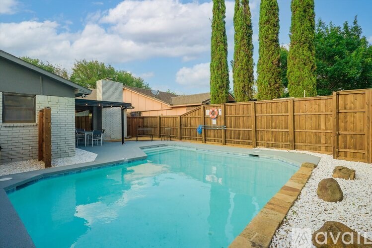 A pool surrounded by a wooden fence and a house with a patio.