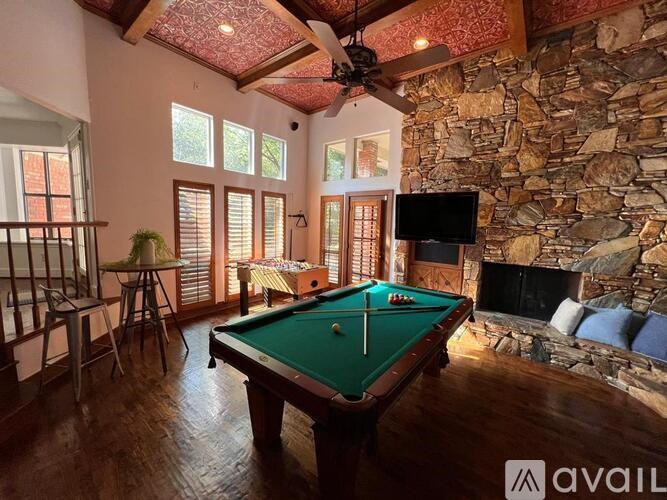 A pool table in a room with a stone fireplace and a ceiling fan.