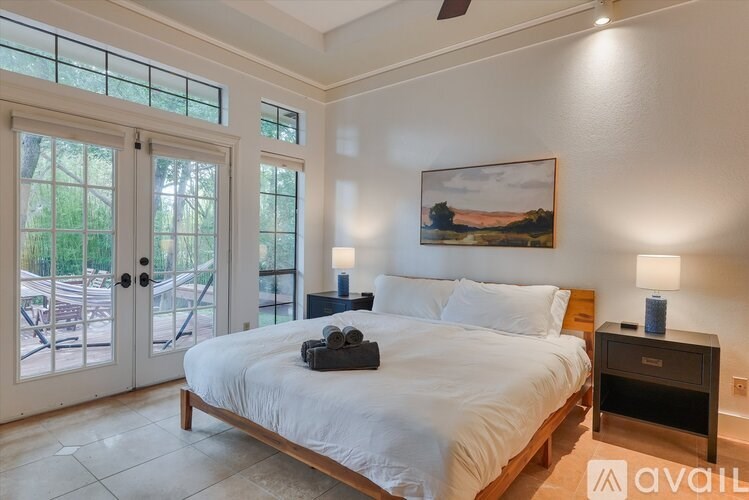 A bedroom with a large bed, a ceiling fan, and a painting on the wall.