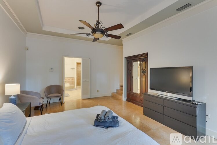 A bedroom with a bed, a chair, a table, a ceiling fan, and a television.