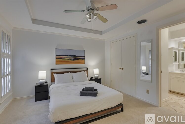 A bedroom with a large bed, a ceiling fan, and a painting on the wall.