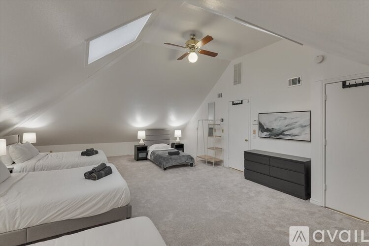 A bedroom with a skylight, a bed, a dresser, and a painting on the wall.