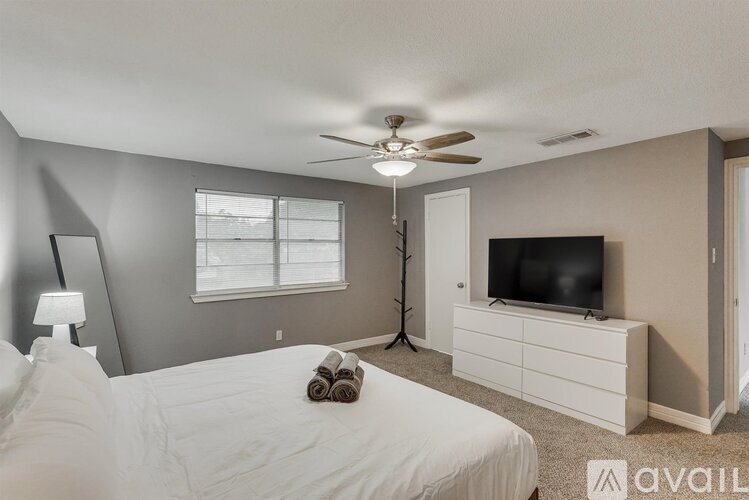 A bedroom with a bed, a ceiling fan, a television, and a window.