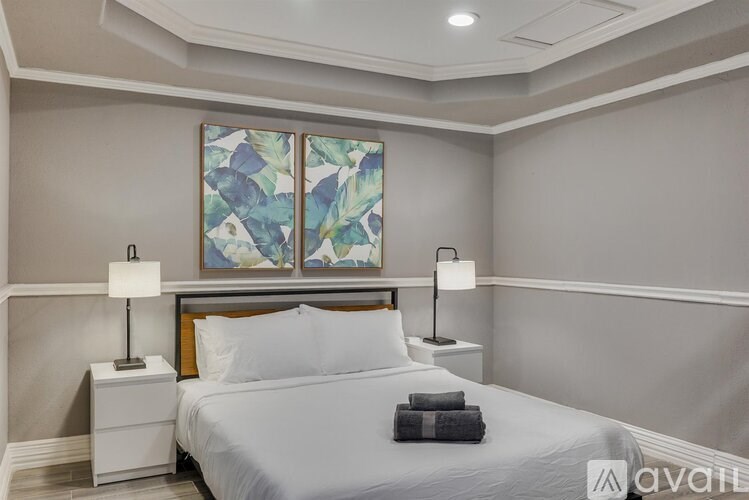 A bedroom with a large bed, two lamps, and a painting on the wall.